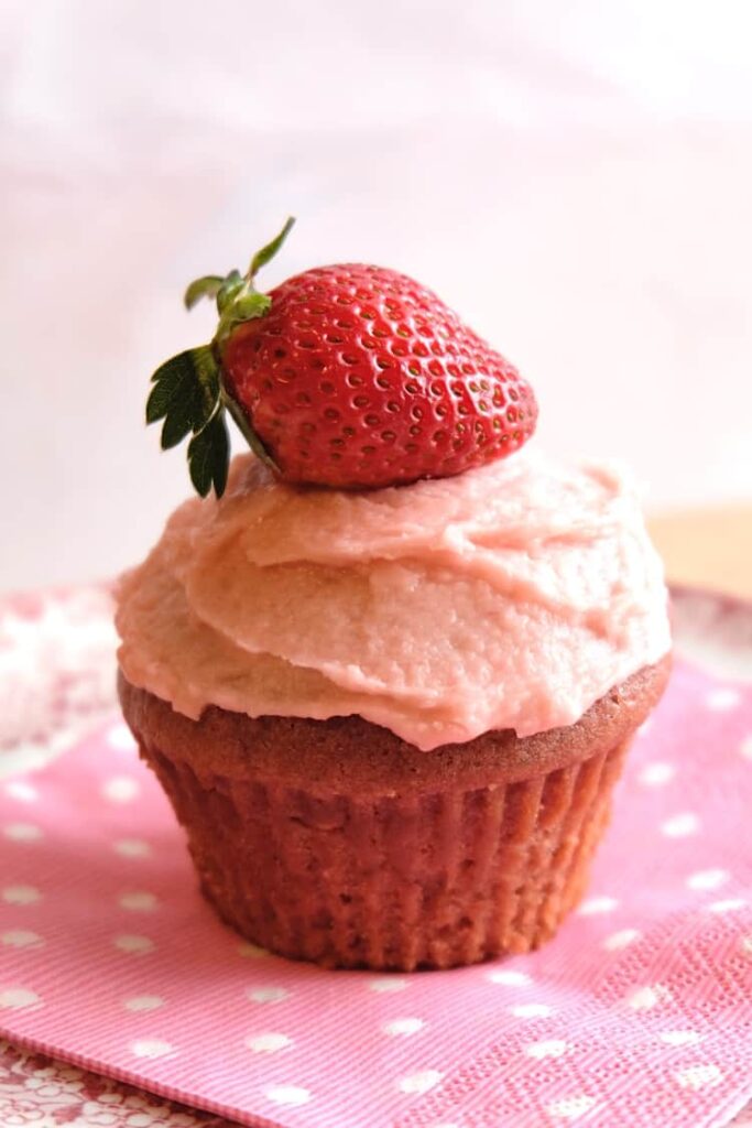 Vegan strawberry cupcake with strawberry icing and a fresh strawberry on top.