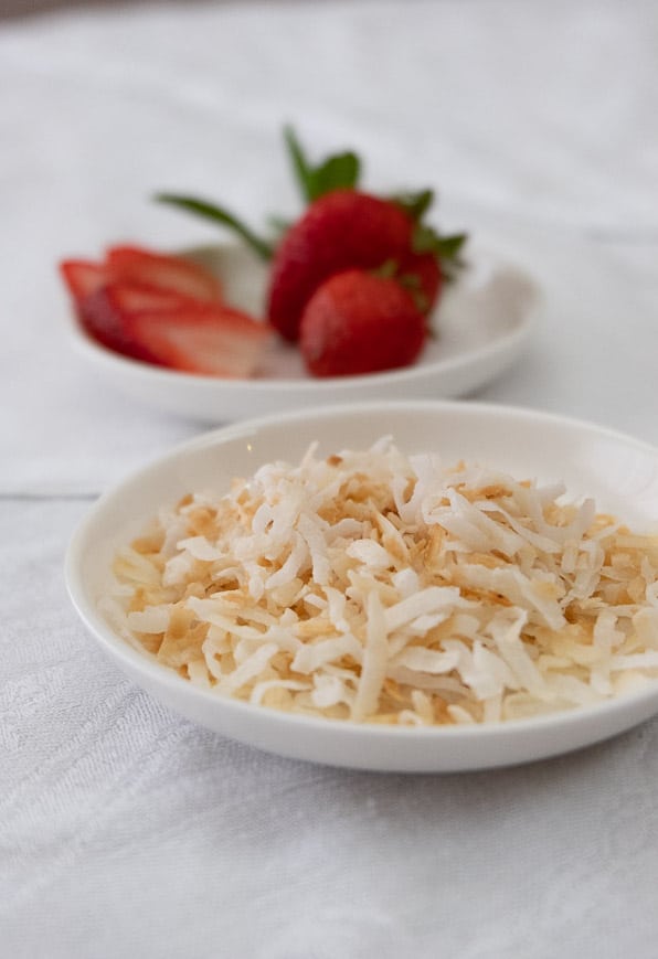 Shaved coconut flakes and slices of strawberry as vanilla coconut milk ice cream toppings.