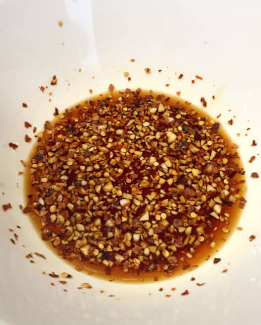 A marinade liquid containing soy sauce, chili flakes, and garlic.
