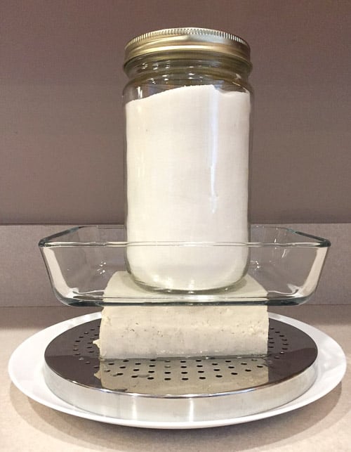 pressing water out of tofu using a heavy jar of salt to weigh down on the tofu.