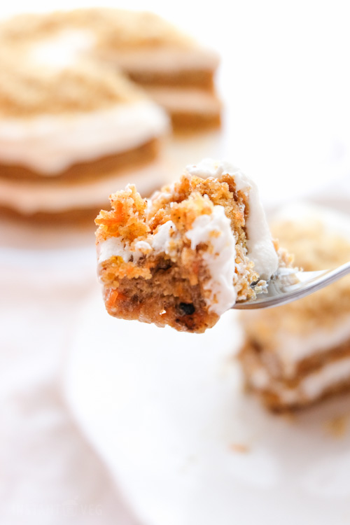 A close-up image of a bite size piece of carrot cake with frosting on a fork.