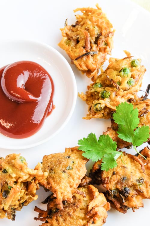 Fried vegetable dumpling (pakora) on a plate with ketchup and garnished with cilantro.