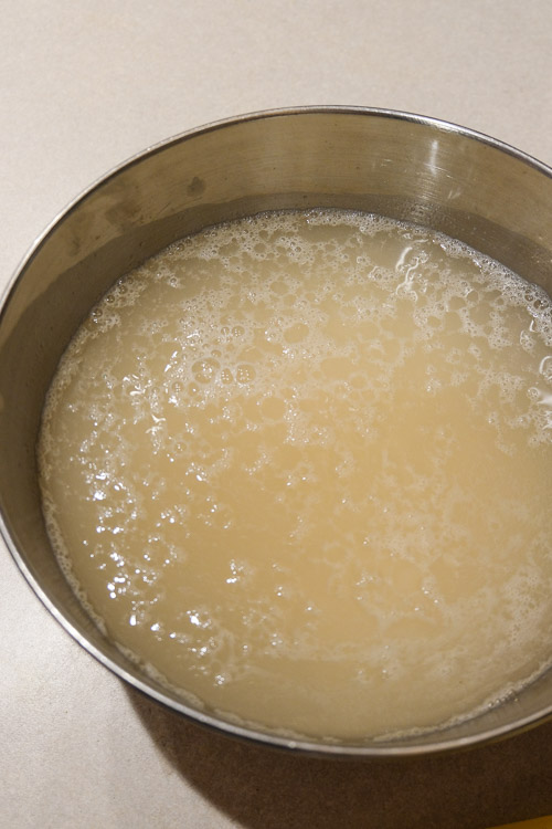 A bowl containing water and grated potatoes, with starch visible on the surface of the water.