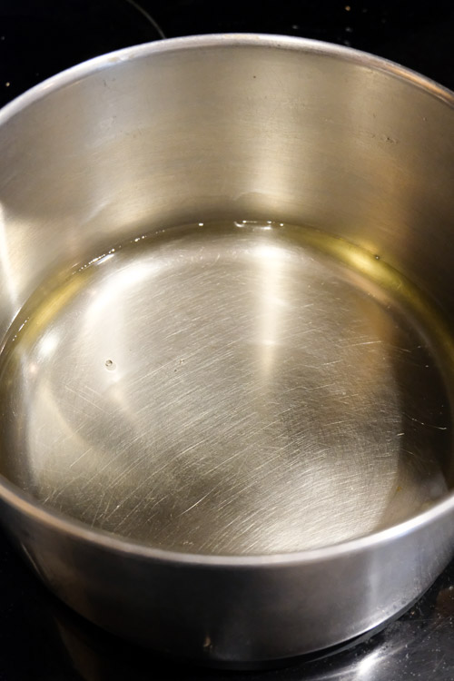 A metal saucepan containing about one inch of vegetable oil, heating up on a stove.