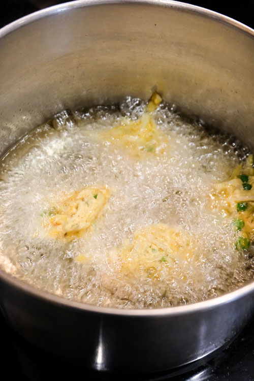 Spoonfuls of pakora mixture being fried in the hot oil, with lots of air bubbles boiling to the surface.