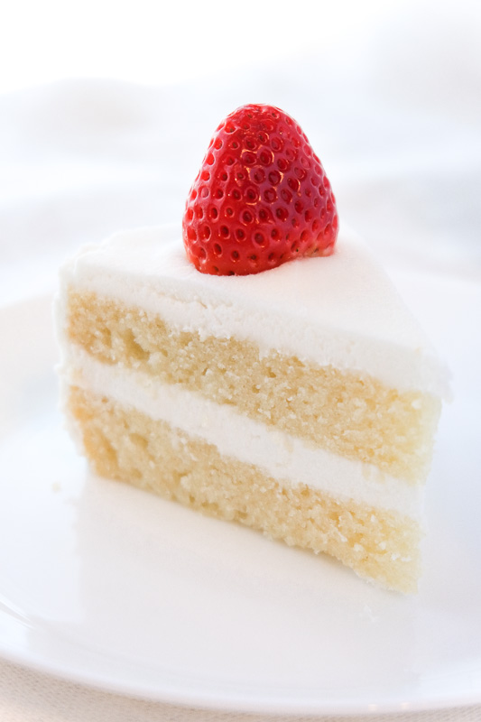 A white vegan vanilla cake slice with white frosting and strawberry.