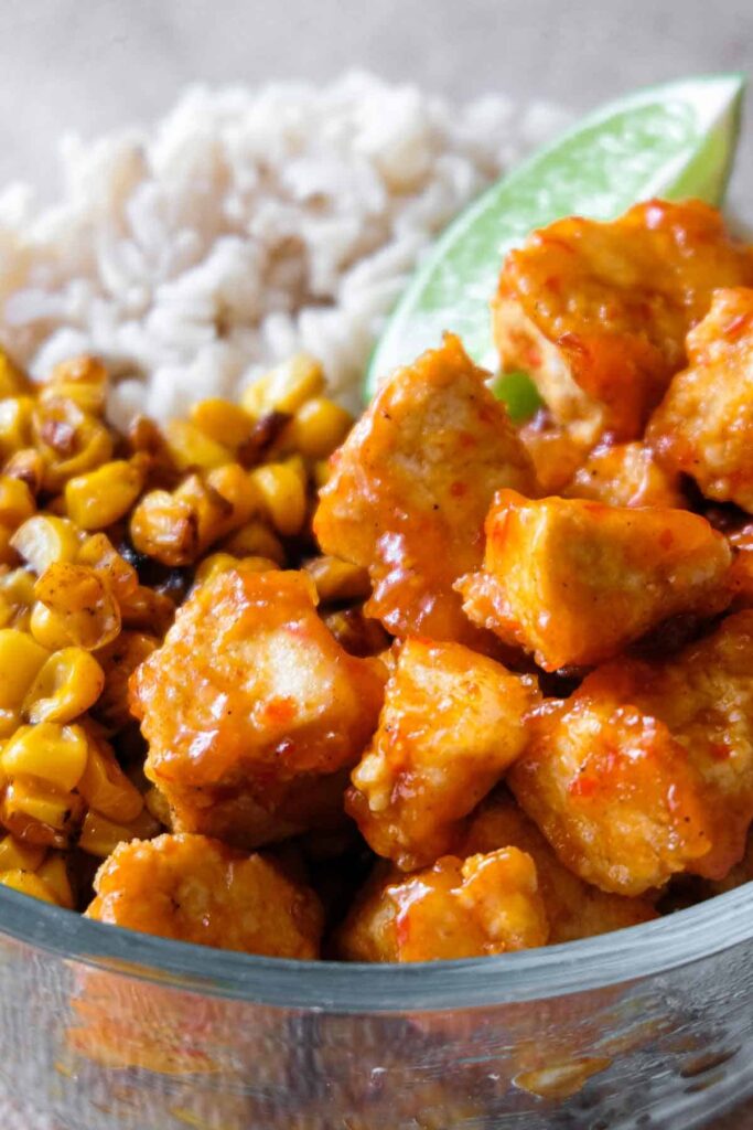 close up view of tofu, corn, riec, and a lime in a bowl.