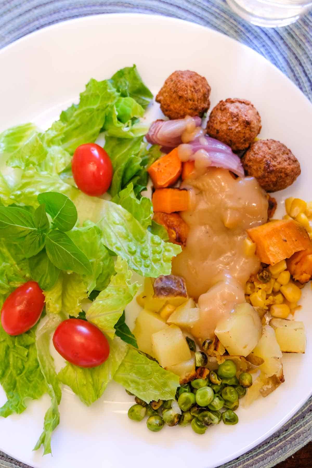 Vegan roasted vegetables and gravy on a plate with salad.