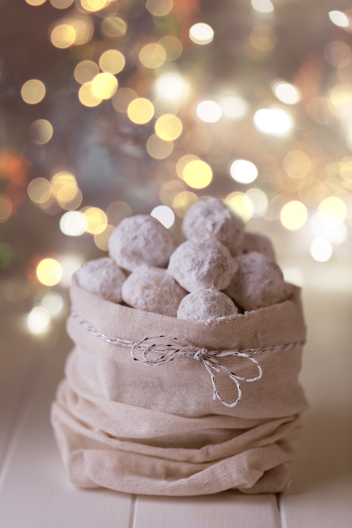 Vegan snowball cookies in a cute sack with Christmas lights in the background.