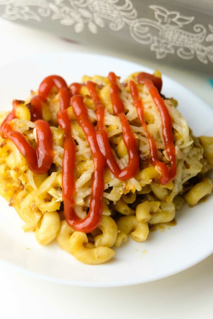 A portion of baked vegan macaroni and cheese on a plate with ketchup.