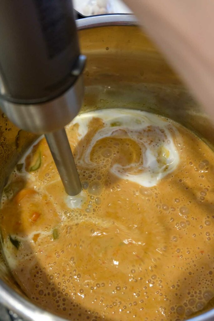 Blending the cooked veggies and coconut milk using an immersion blender.