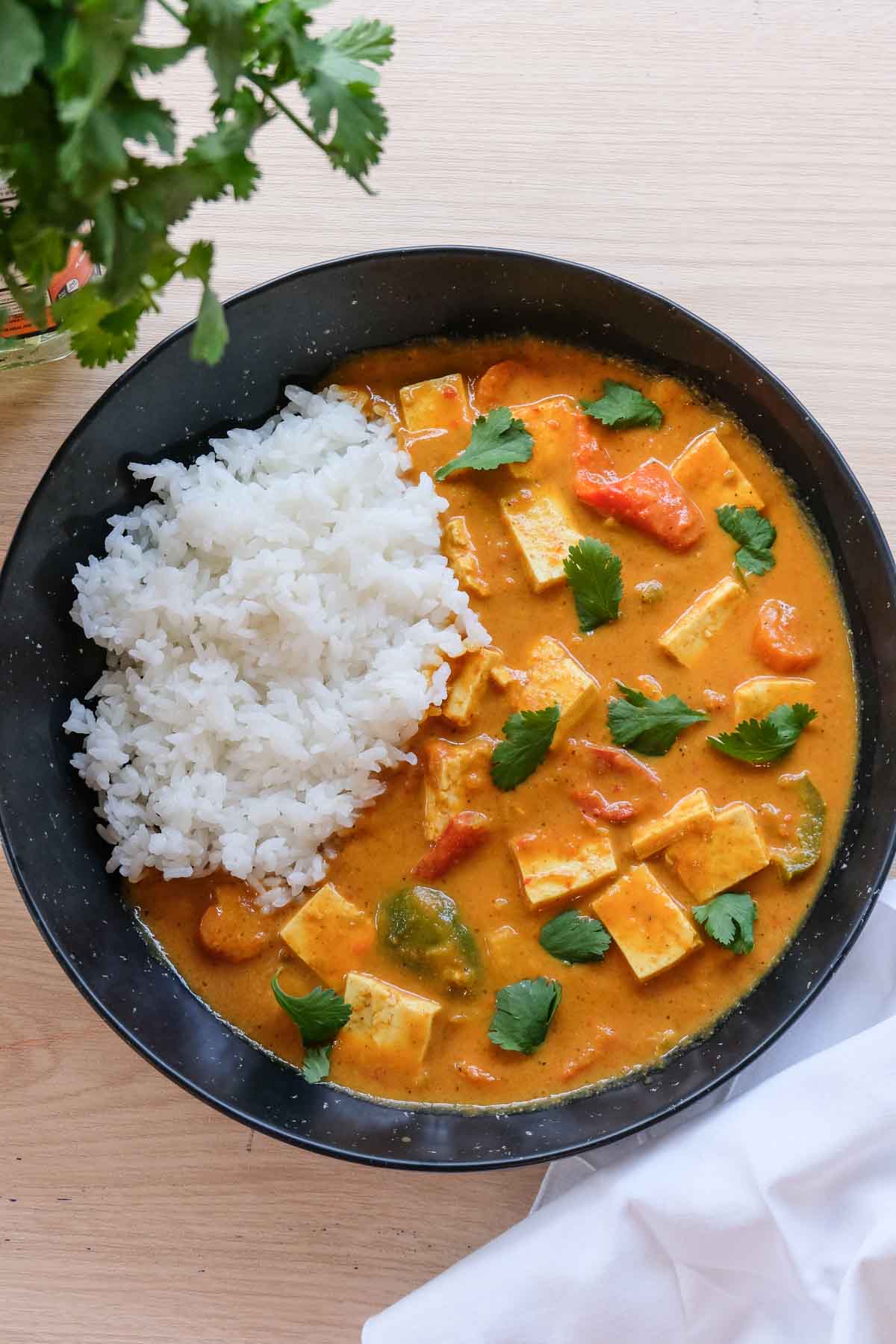 A plate of vegan butter chicken made from tofu, garnished with cilantro, with rice on the side.