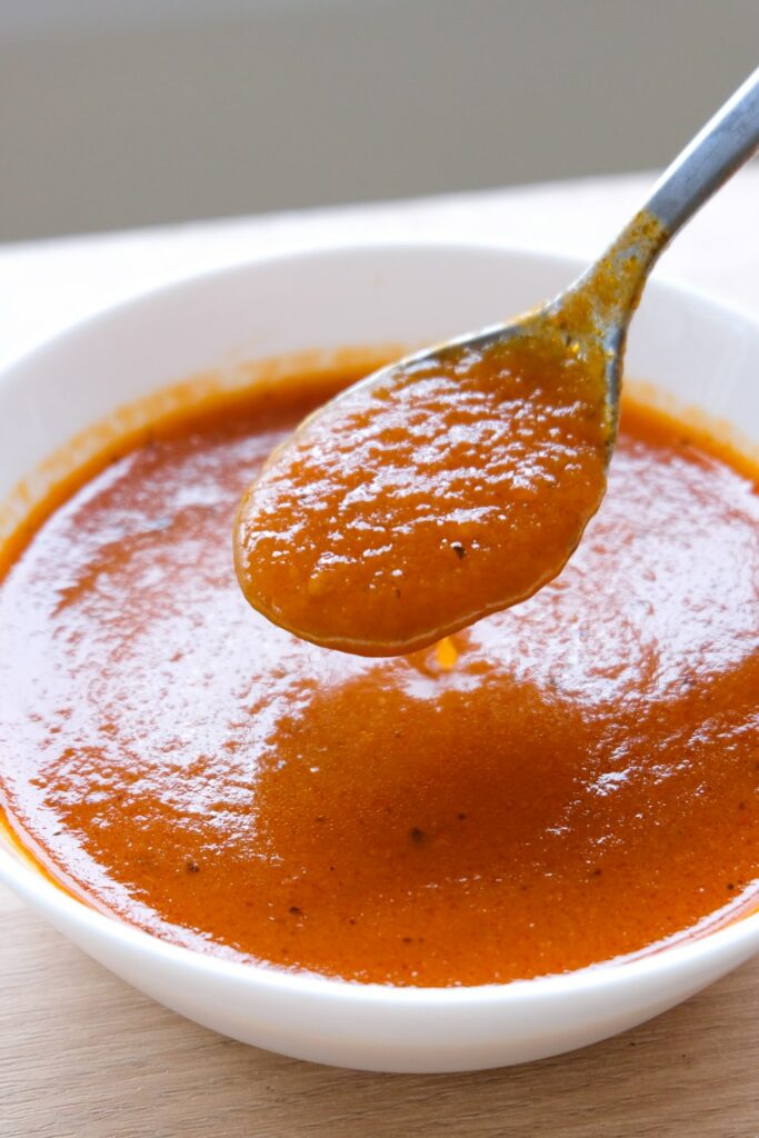 close up view of tomato soup in a bowl being scooped up in a spoon.