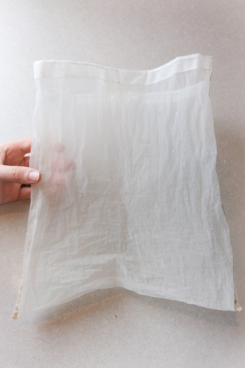 A hand holding a nut milk bag on a counter.