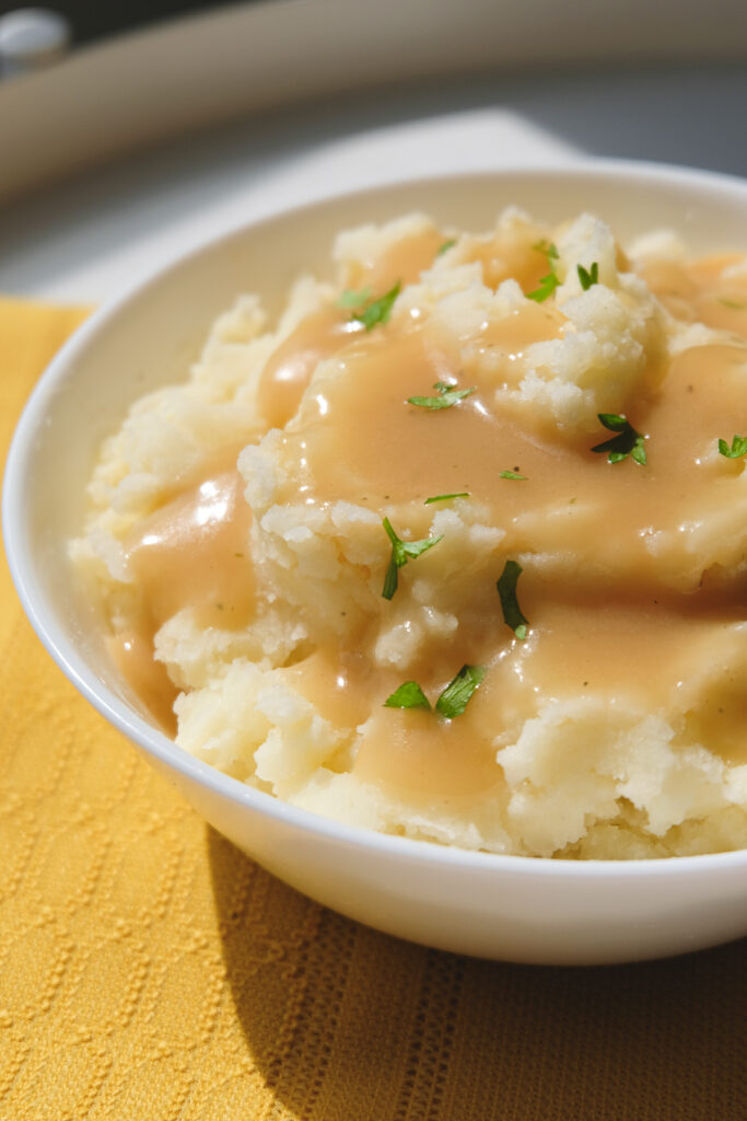 Close-up view of gravy poured over a bowl of mashed potatoes garnished with flakes of fresh parsley.