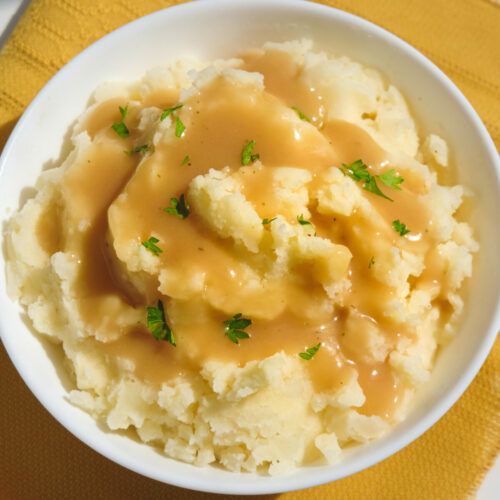 Vegan gravy poured over a bowl of mashed potatoes, garnished with parsley.