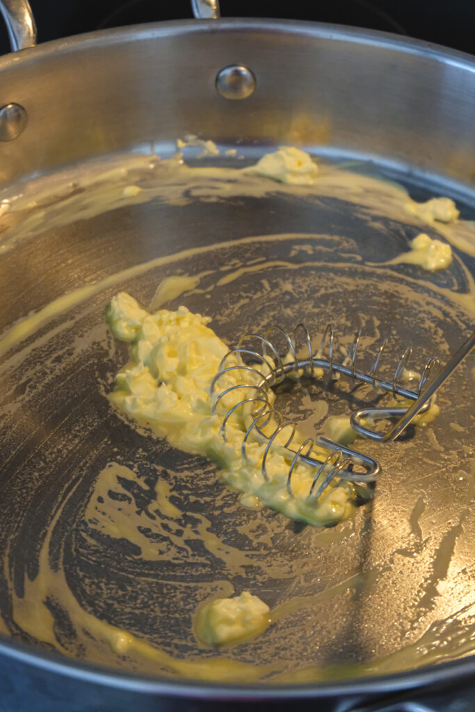 Vegan butter being stirred with a whisk in a frying pan as it melts.