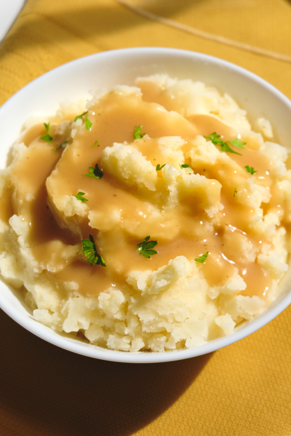 Vegan gravy poured over mashed potatoes in a bowl on a yellow tablecloth.