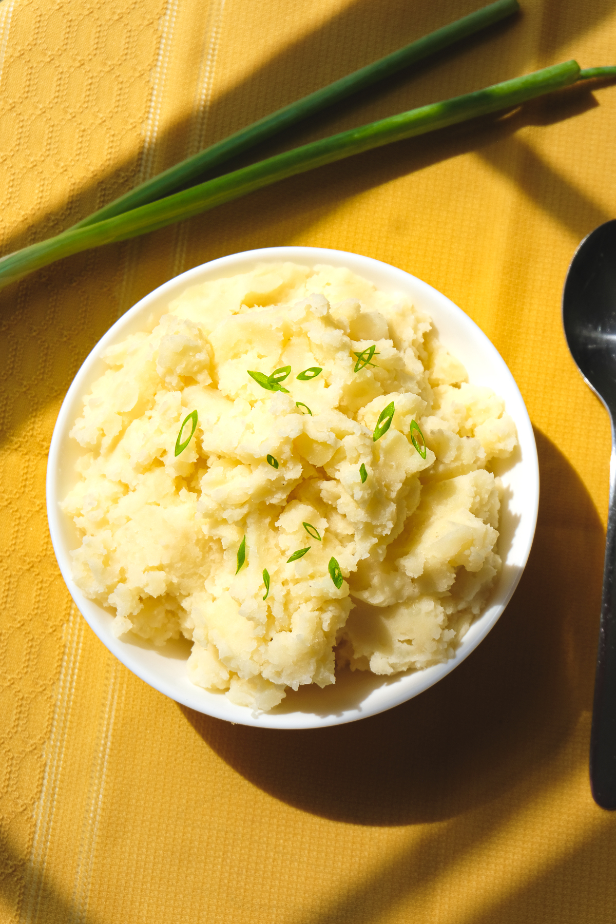 Vegan Mashed Potatoes in a bowl on a yellow cloth with green onions.