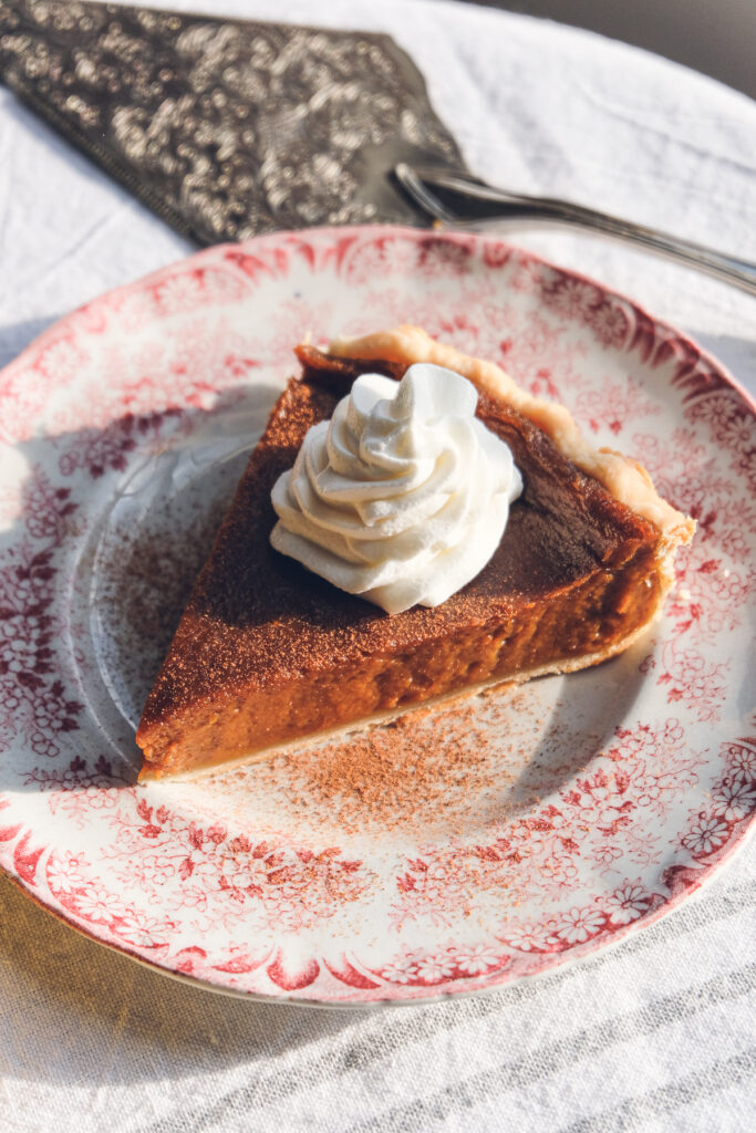 A slice of vegan pumpkin pie on a plate, topped with a spiral of whipped cream.