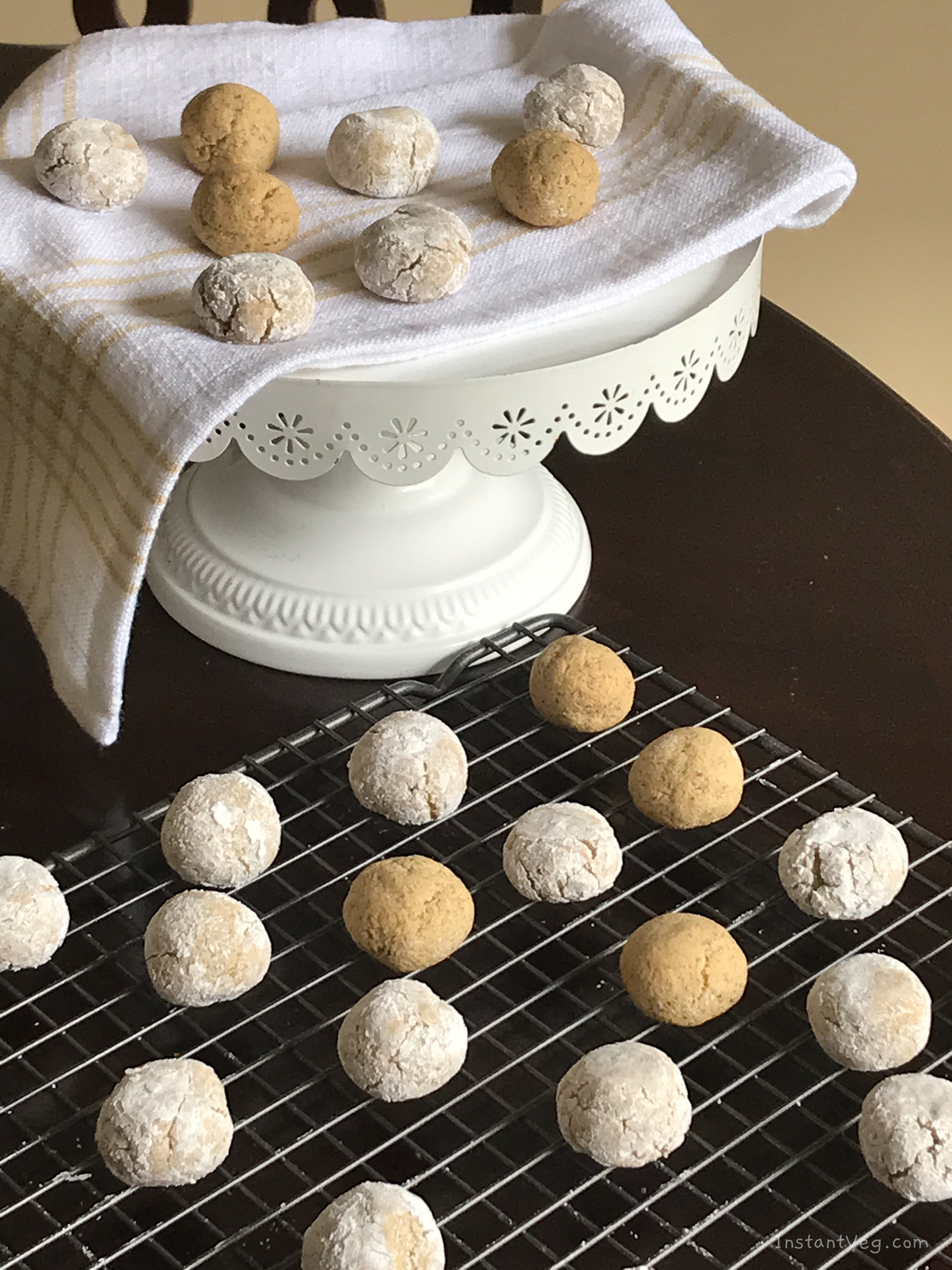 small white and golden round cookies on a baking sheet and on a towel-laden cake stand.