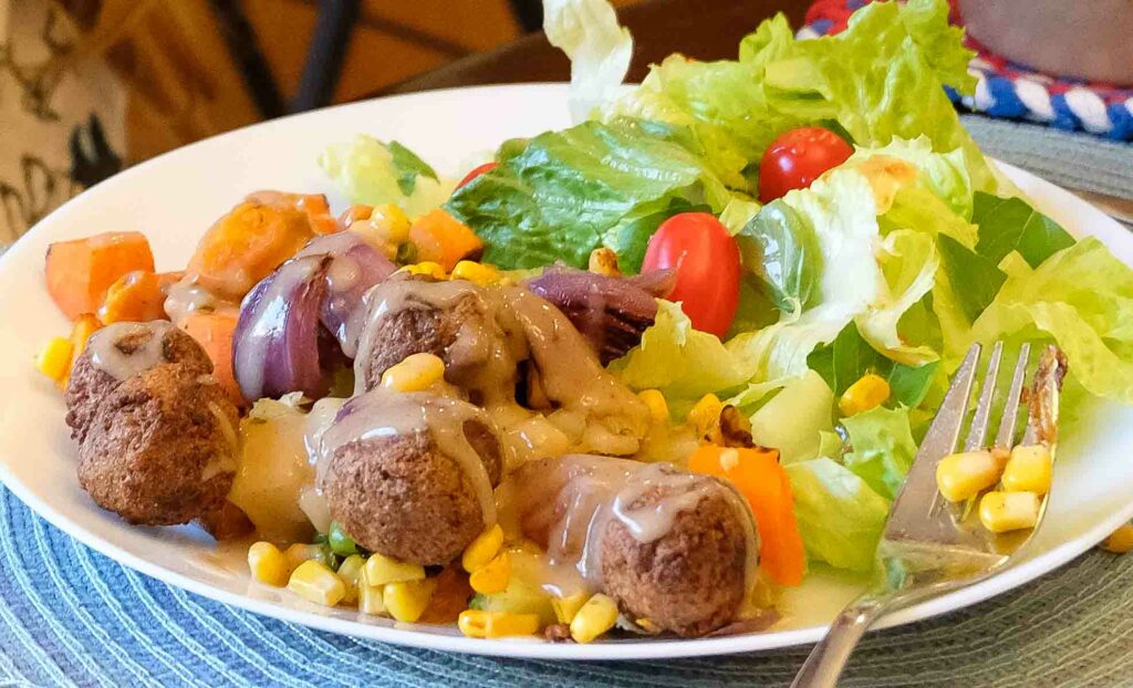 Vegetable roast with vegan meatballs and gravy, with a side salad.